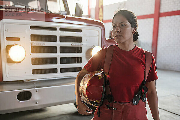 Portrait of female firefighter looking away standing at fire station