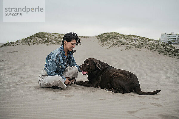 Woman Sitting with Dog on Sandy Beach