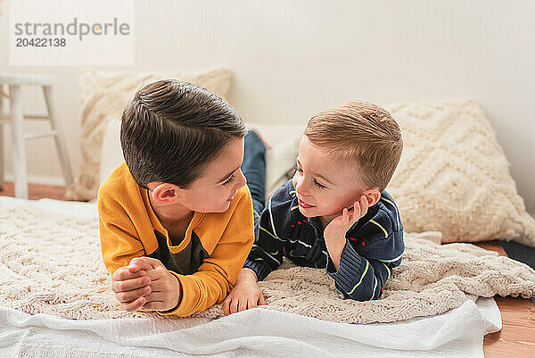 Two smiling brothers lying on a blanket and talking