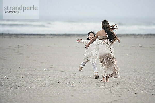 Young girl running to hug her pregnant mother on a cloudy beach