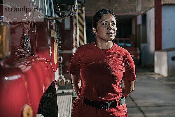 Portrait of female firefighter looking away standing at fire station