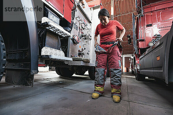 Female firefighter wearing fire protection suit against fire engine