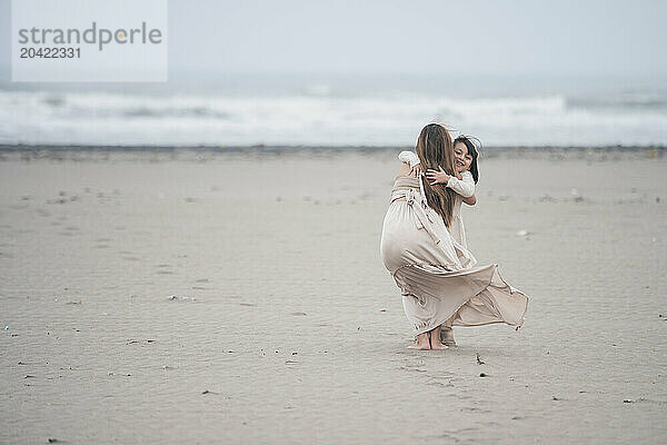 Young girl joyfully hugging her pregnant mother on a cloudy beach