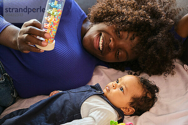 African mother is playing with a toy with her baby girl on a sofa.