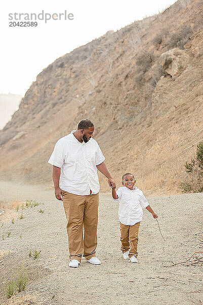 Father and son holding hands walking down a path with hills in t