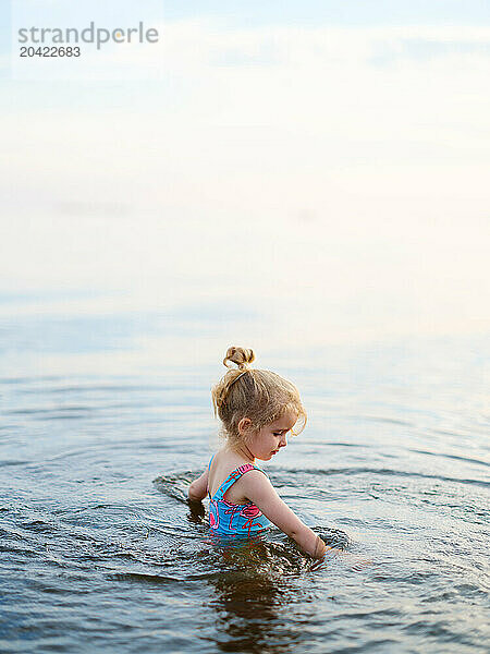 Funny little girl splashes and swims in lake water in summer