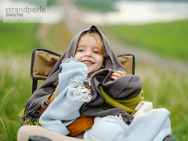 Smiling little girl wrapped in a blanket sits on a chair