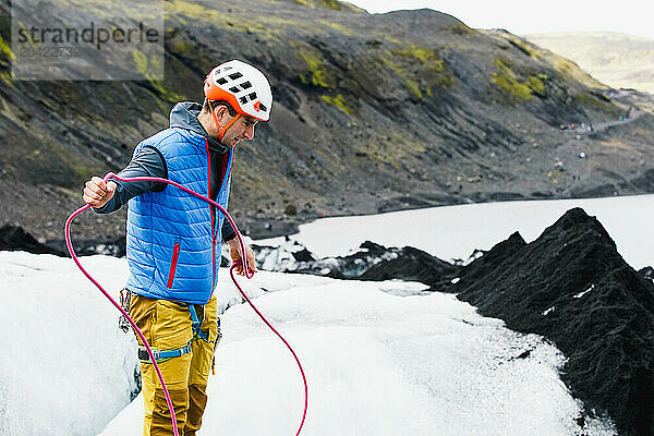 Young man in colourful clothes swings a rope on an Icelandic glacer