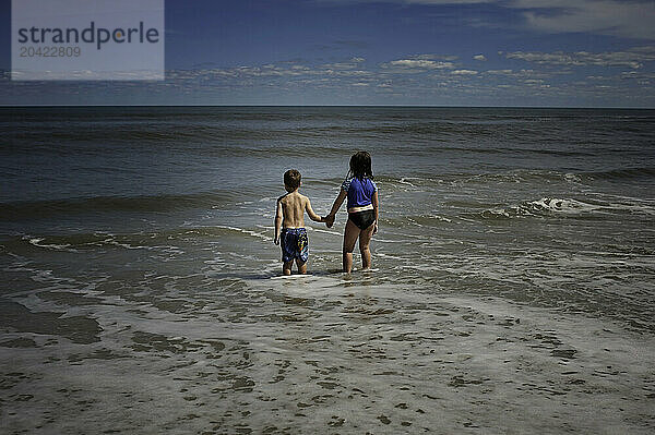 Young children holding hands at beach in waves under blue sky