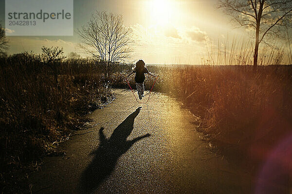 Young girl jumping rope down path near sunny field