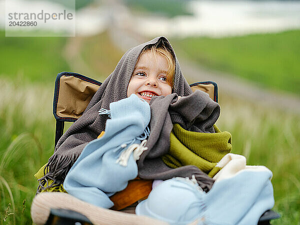 Smiling little girl wrapped in a blanket sits on a chair