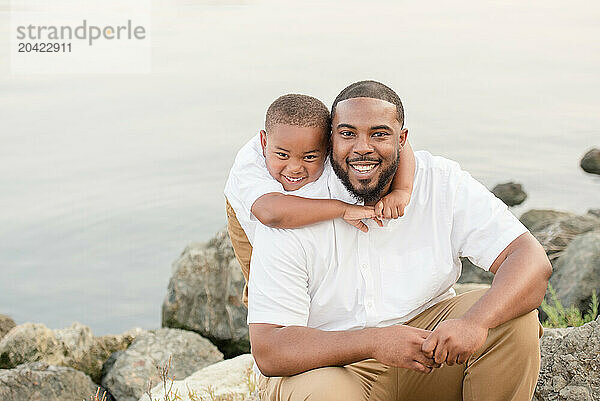 Son putting arms around fathers neck smiling outside