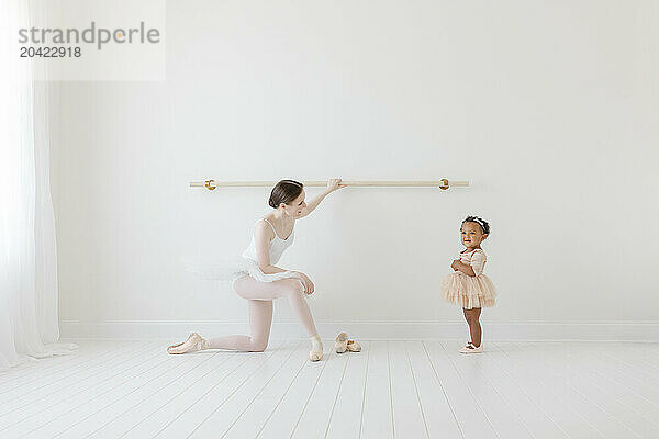 Adult Ballerina shows BIPOC baby ballet barre in white studio