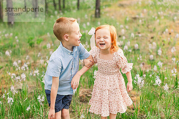 Joyful siblings laughing together in a wildflower field