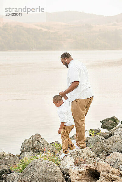 Father and son walking on the rocks holding hands by the water