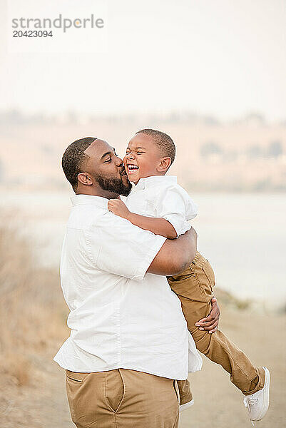 Father holding son giving him a kiss on the cheek laughing