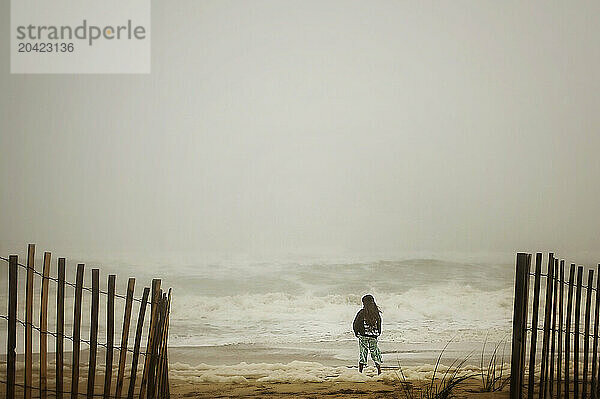 Young girl standing in sand on stormy beach with big waves