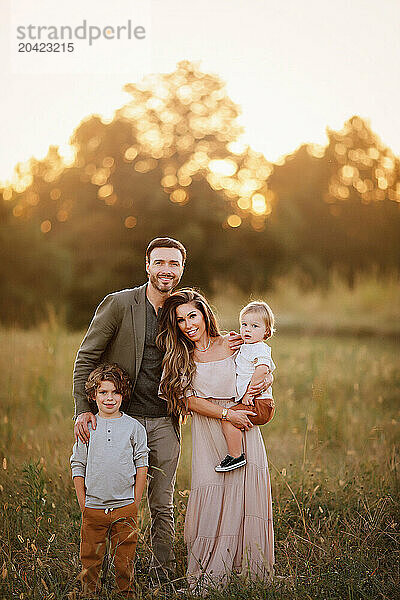 Family of four standing together in a grassy field at sunset  sm