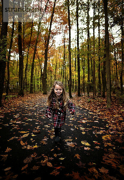 Happy young girl running down path with colorful leaves and trees