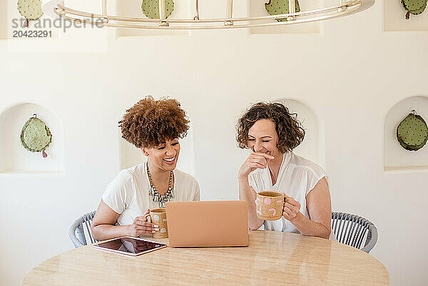 Two women working on laptop laughing