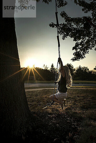 Little girl long blonde curls swinging in bright sunlight