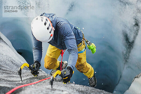 A man climbs up a glacier crevasse with ice axes