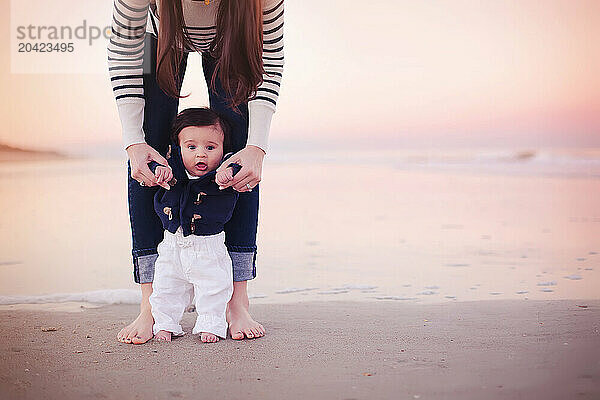 Mother holding her baby upright on the beach at sunset  baby loo