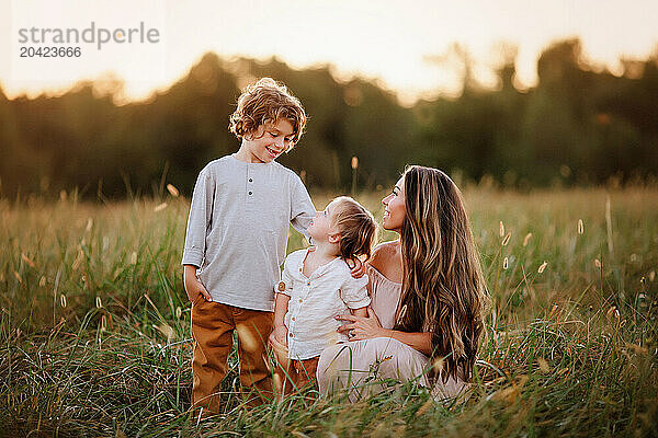 Mother kneeling in a grassy field with her two young children at