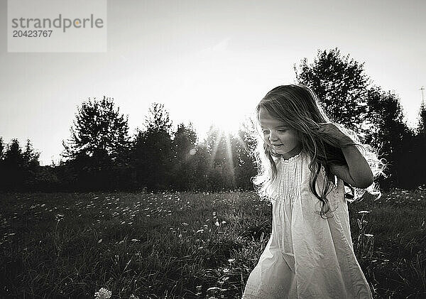 Happy little girl holding hair walking through flower field