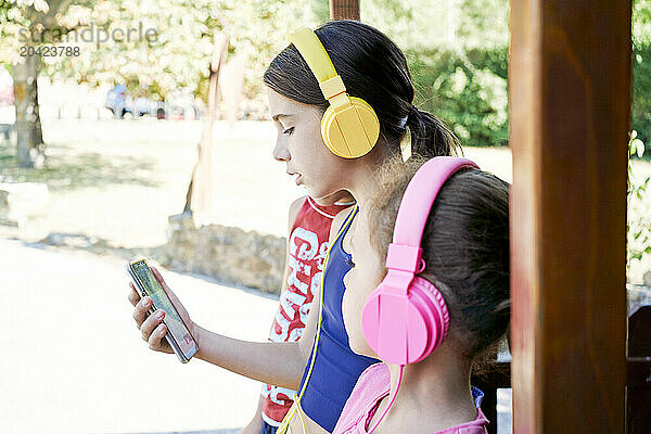 side view of two girls standing in a park with headphones