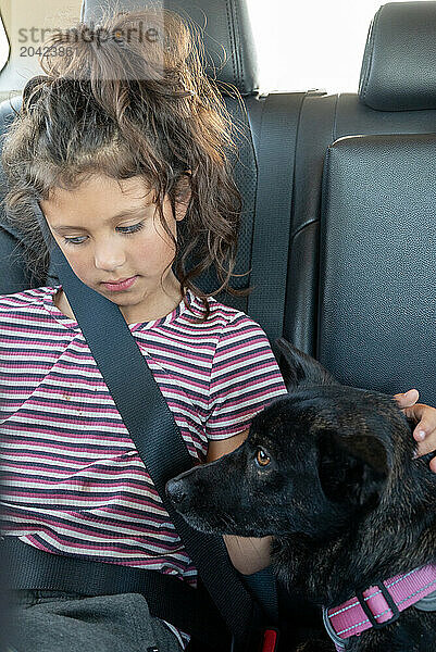 Young hispanic girl and dog in back of car