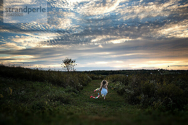 Little girl running in green field with streamer at sunset