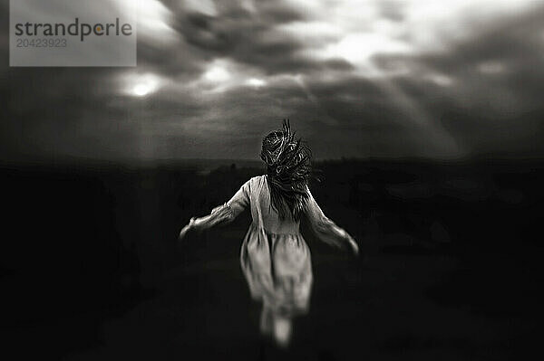 Back view of young girl hair blowing walking towards stormy sky