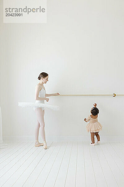 baby ballerina reaches for ballet barre with teacher