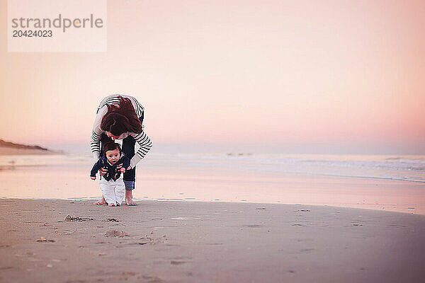 Mother holding her baby on the beach at sunset  baby looking for