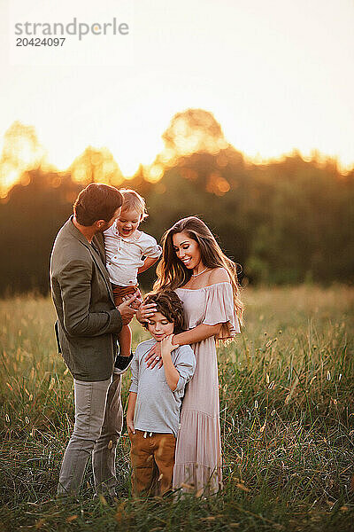 Family of four standing in a grassy field at sunset  interacting