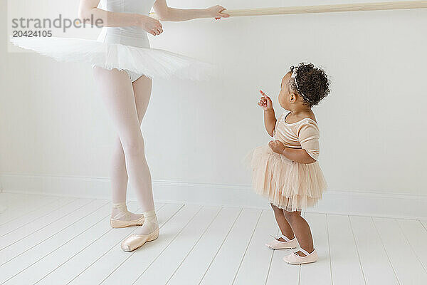 mixed race baby in tutu admires ballerina in ballet studio