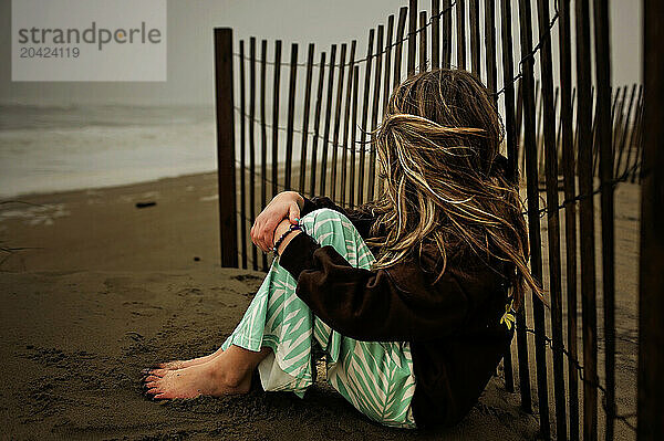 Young girl wind blowing in hair sitting on stormy beach