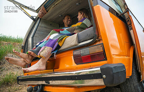 Happy diverse couple sitting in parked van with blanket