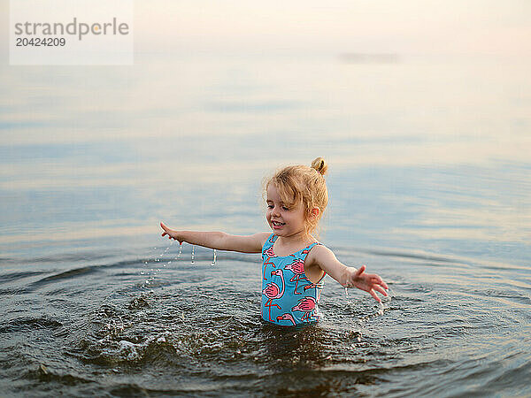 Funny little girl child splashing in lake water in summer