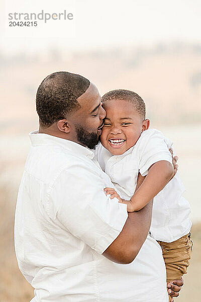 Father giving son a kiss on the cheek holding him and laughing