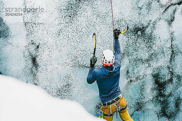 Man hits an ice wall with axe while climbing up an Icelandic glacer