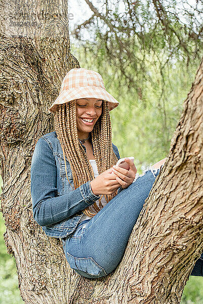 Teenage girl sitting in tree looking at cell phone