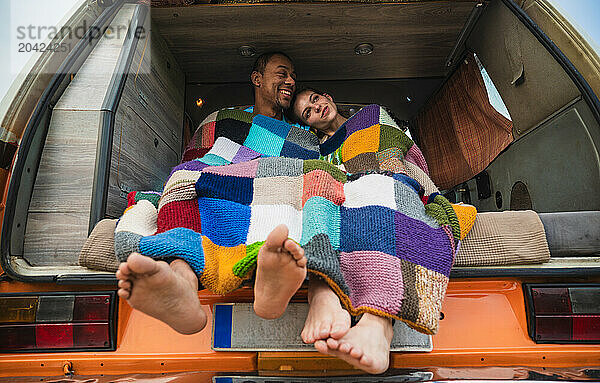 Happy diverse couple sitting in parked van in daylight