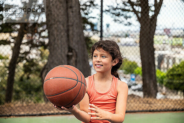 Young hispanic girl holding basketball on court in San Francisco