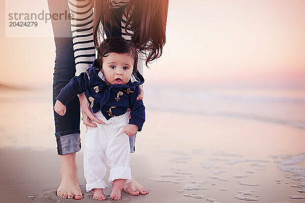 Mother holding her baby on a beach at sunset  baby's feet touchi