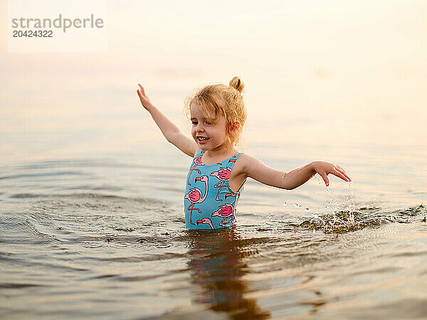 Funny little girl child splashing in lake water in summer