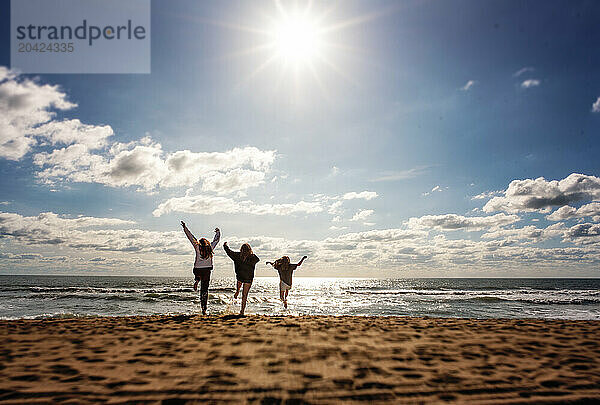 Three young girls running and jumping on sunny beach