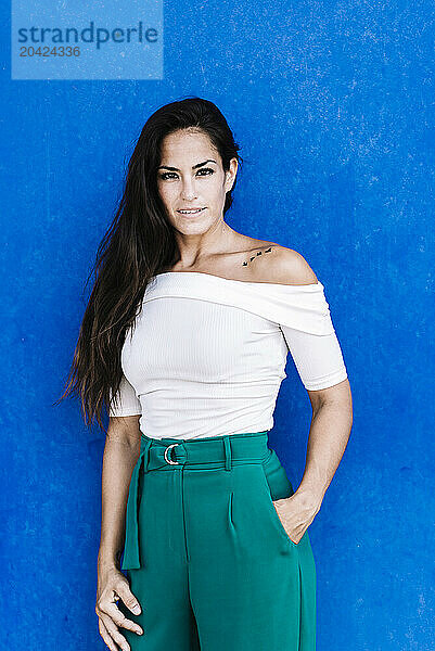 Portrait confident smiling young woman against a blue wall