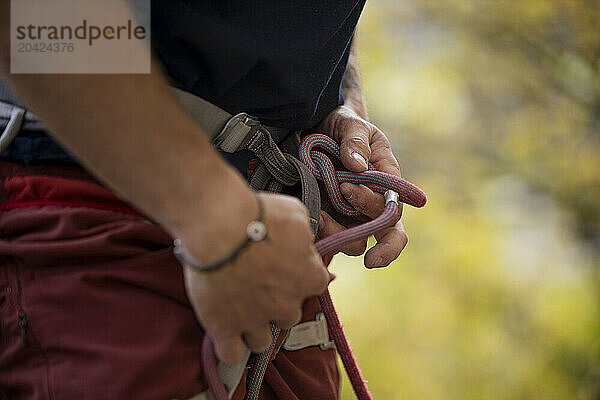 Man tying climbing knot with autumn tree background